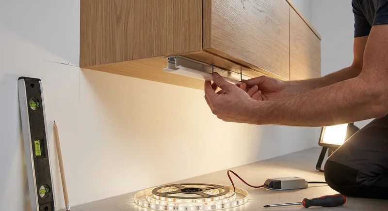 Montaż aluminiowego profilu LED pod szafką. Na blacie leży świecąca taśma i narzędzia.
